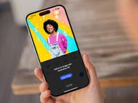 A person holding a smartphone displaying Adobe Photoshop app with colorful graphic design.