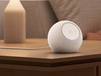 A white Amazon Echo Dot Max speaker on a wooden table next to a lamp.