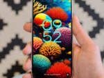 A hand holding a Google Pixel 9 smartphone displaying a colorful coral-themed wallpaper and the time 09:52.