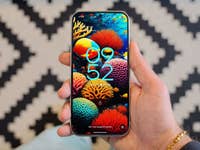 A hand holding a Google Pixel 9 smartphone displaying a colorful coral-themed wallpaper and the time 09:52.