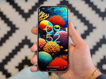 A hand holding a Google Pixel 9 smartphone displaying a colorful coral-themed wallpaper and the time 09:52.