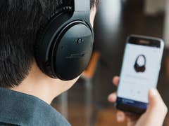 A Bose headphone highlighted with smartphone screen blurred in the background.