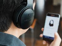 A Bose headphone highlighted with smartphone screen blurred in the background.