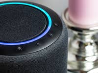Close-up of a smart speaker with blue ring light and controls, next to a pink candle.