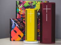 Two Ultimate Ears speakers, one yellow and one red, with colorful boxes in the background.