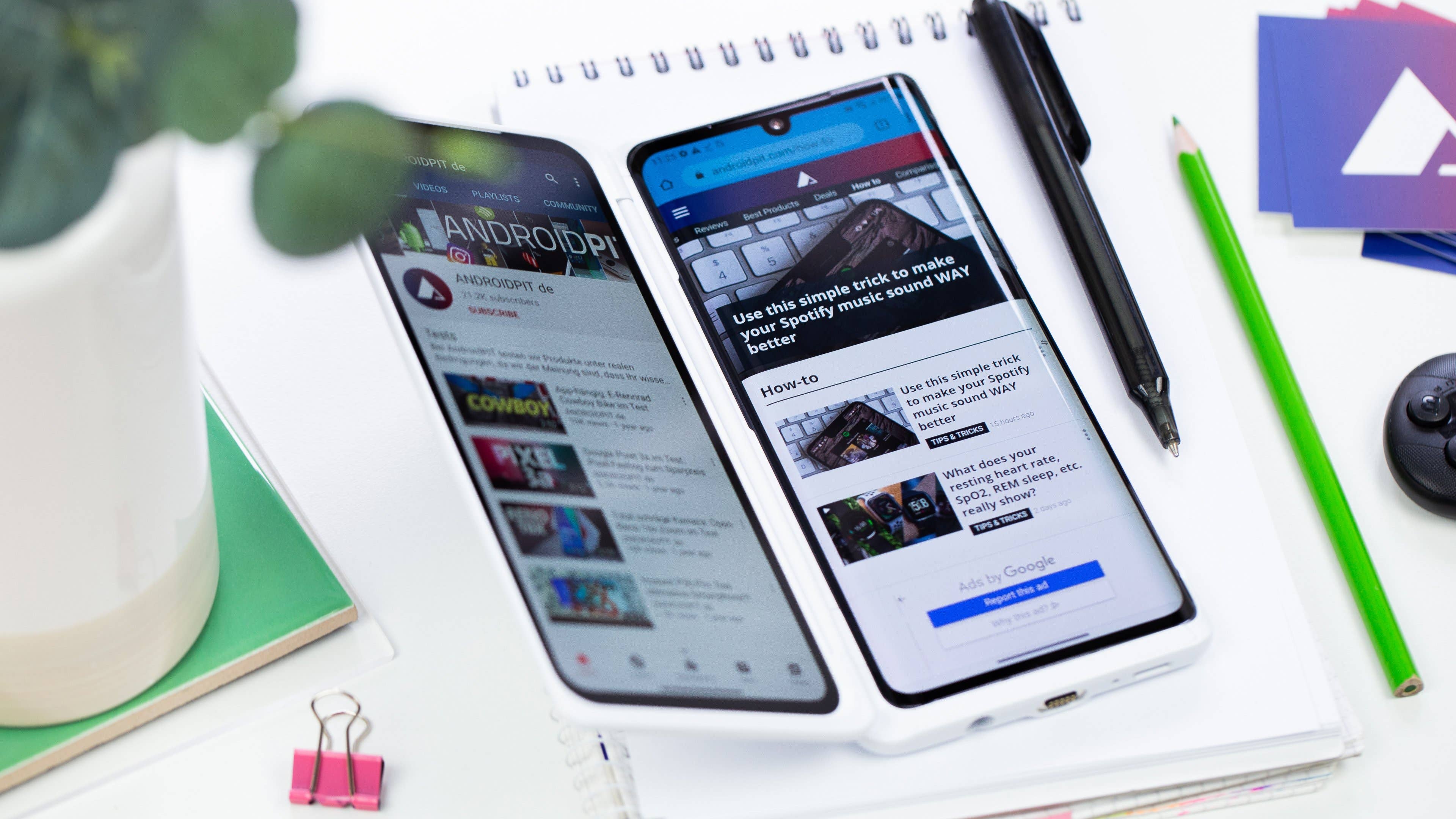 Two smartphones displaying websites on a desk with a notebook, a plant, and stationery. Two smartphones displaying websites on a desk with a notebook, a plant, and stationery.