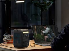 A portable Anker Solix C200 X power station on a desk, connected to a laptop, with a man working in the background.