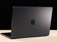 A black Apple MacBook Pro laptop viewed from the back on a light surface.