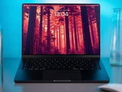 A MacBook Pro on a desk displaying a forest wallpaper with the time 13:04.