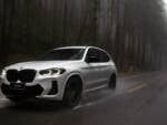 A white BMW X3 driving on a wet road through a foggy forest.