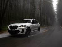 A white BMW X3 driving on a wet road through a foggy forest.