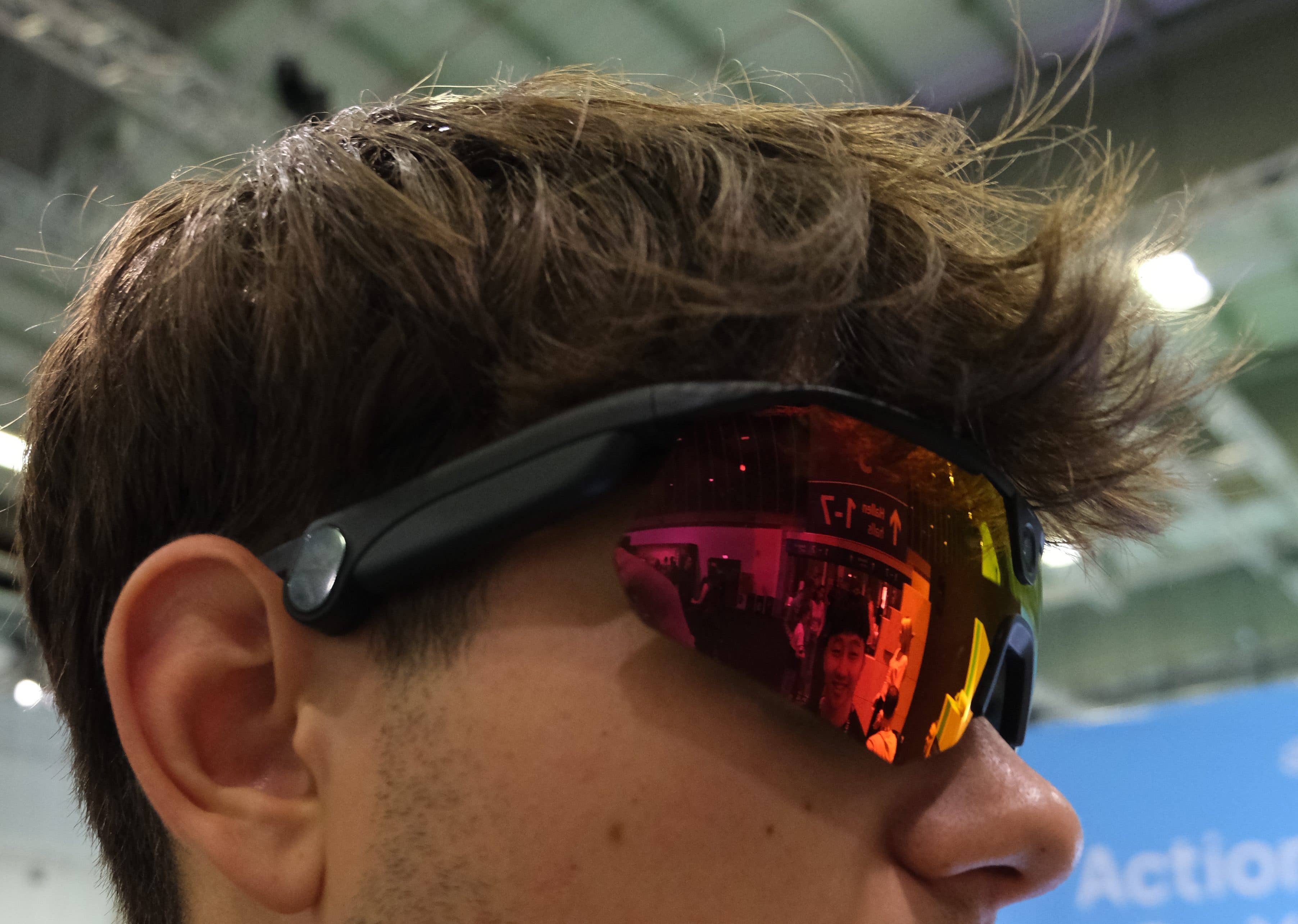 A close-up of a person wearing sunglasses with reflective lenses, showcasing a colorful background.