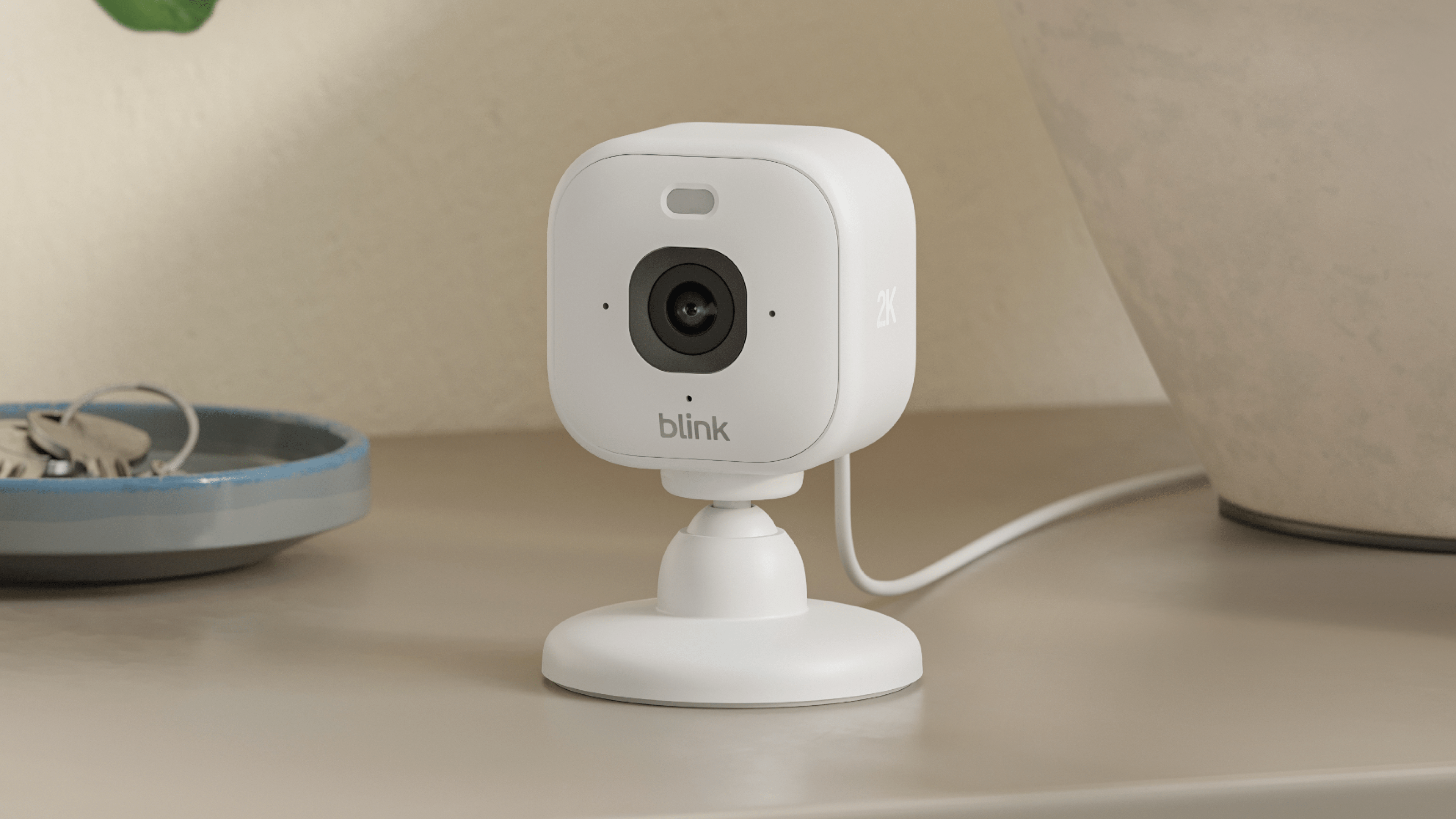 A Blink Mini 2K+ security camera on a table next to a dish with keys.
