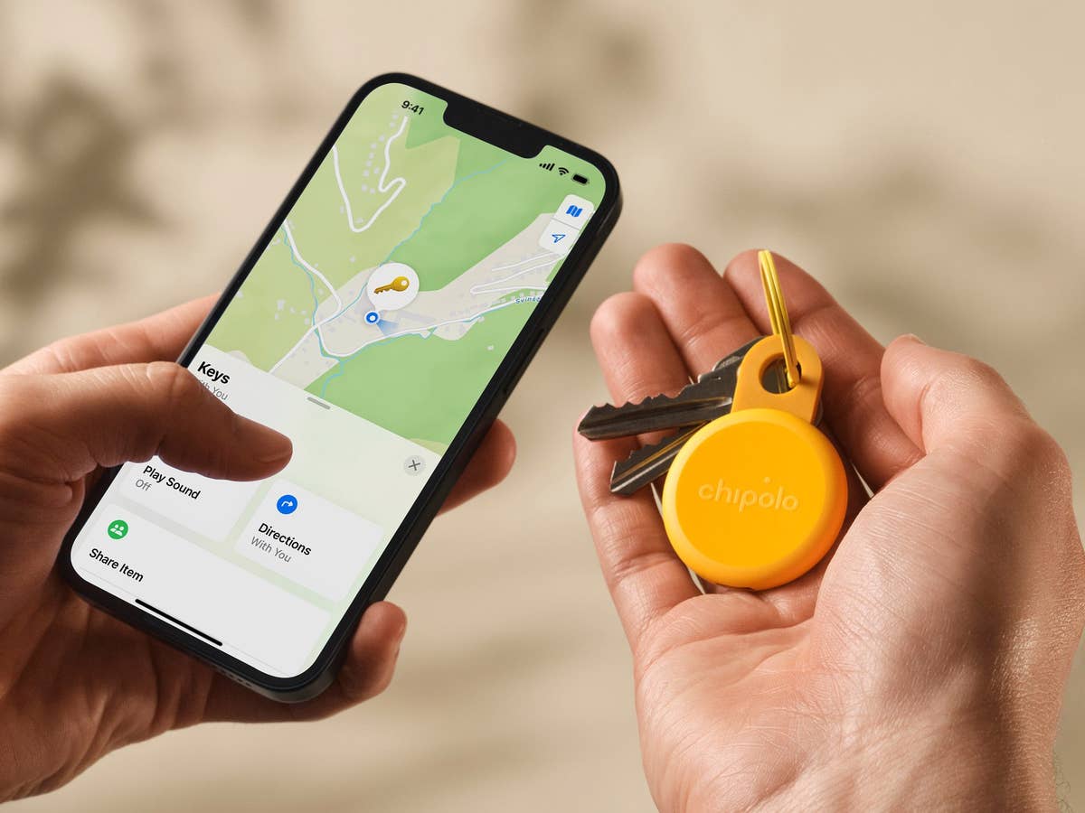 A hand holding a smartphone showing a map with a Chipolo Loop item tracker and keys.