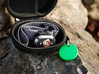 A black zippered case on a rock containing a headlamp and a green Chipolo-Pop tracking tag.