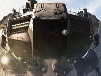 A large futuristic vehicle stands on a beach, surrounded by rocky terrain under a clear sky.