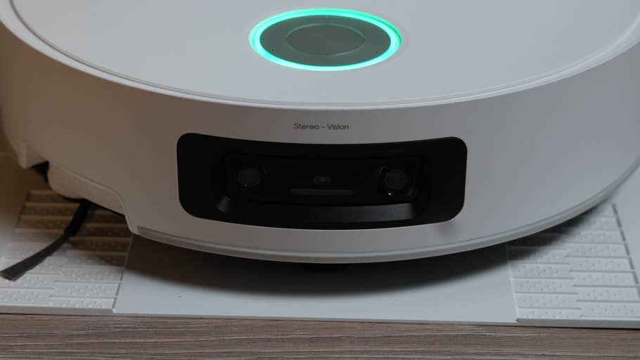 A white robot vacuum cleaner with green light and stereo vision cameras on a textured surface.