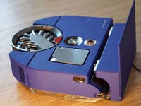 Dyson 360 Vis Nav robotic vacuum cleaner in blue with a sleek design, displayed on a wooden surface.