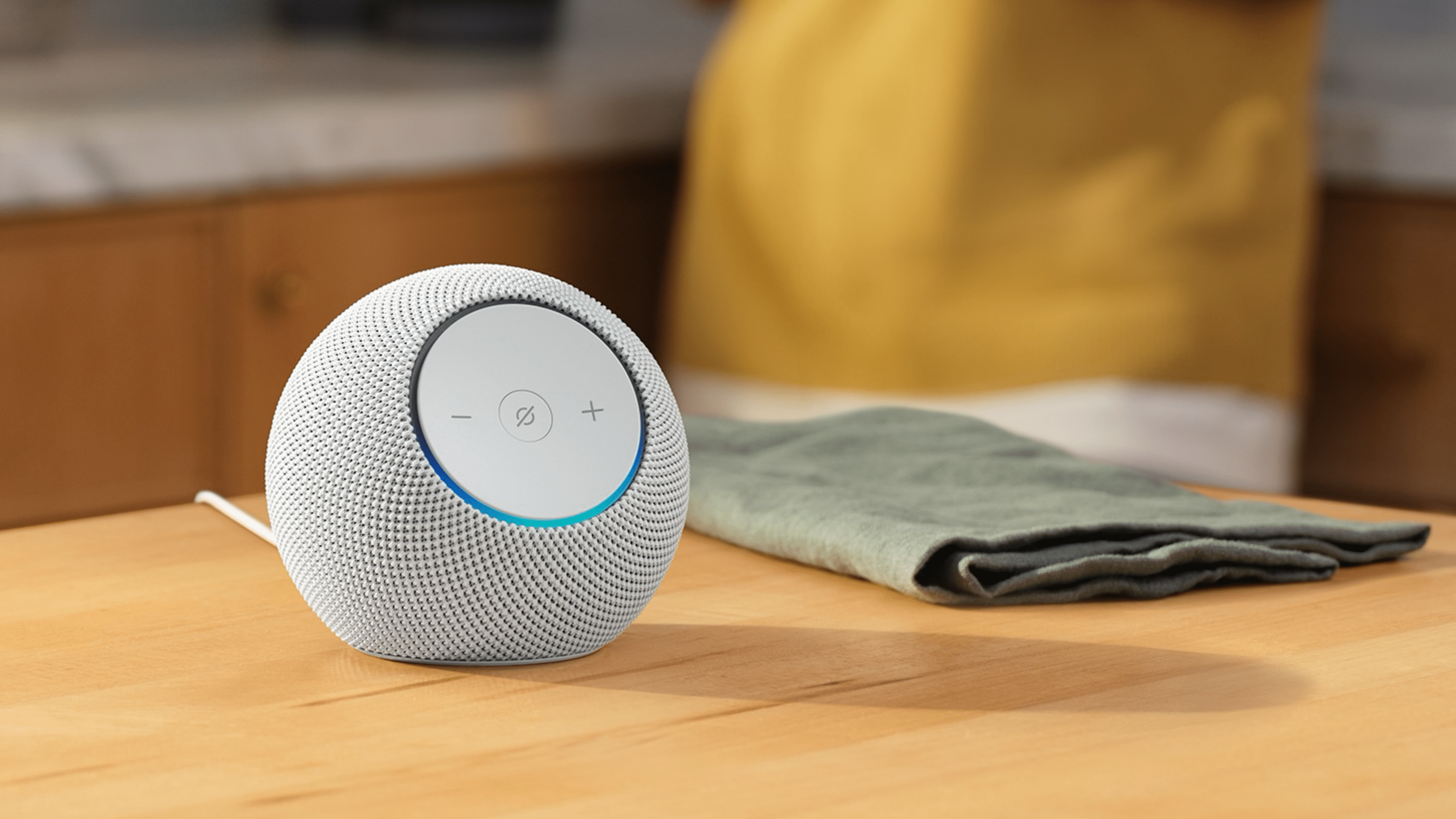 A white Amazon Echo Dot Max speaker on a wooden table with a green cloth nearby.