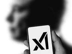 A hand holding a smartphone displaying the 'X' logo against a blurred human silhouette.