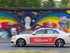 A beige car with a red 'FREENOW' logo drives past a colorful mural.