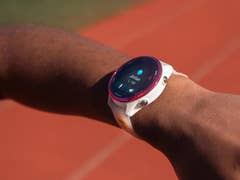 A Garmin Forerunner 570 smartwatch on a person's wrist, displaying a screen with the name 'Jordan' and stats.