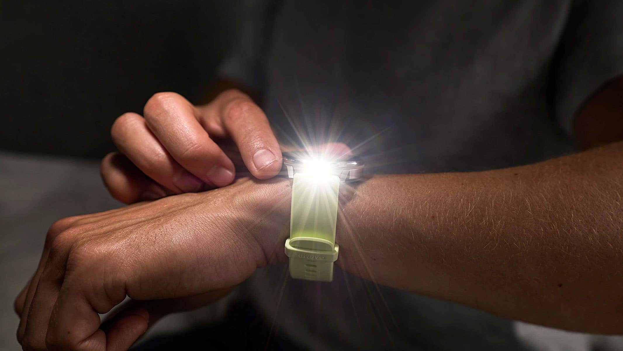 A person adjusts a Garmin Venu 4 smartwatch on their wrist, with a bright light shining from the device.