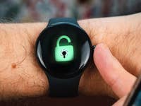 A close-up of a Google Pixel Watch 2 displaying an unlocked padlock icon with a spider.