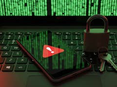 A laptop keyboard with a smartphone displaying a warning symbol and a padlock with keys, set against green code.