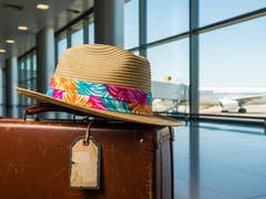 A straw hat on a vintage suitcase at an airport with an airplane in the background.