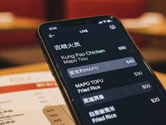 A smartphone displaying a menu with dishes like Kung Pao Chicken and Mapo Tofu, showing prices in a restaurant.