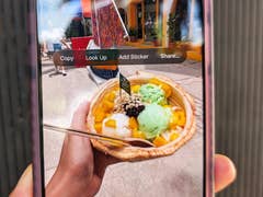 A hand holding a bowl of colorful ice cream with mango, green, and white flavors, displayed on a smartphone screen.