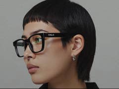 A person with short hair wearing black glasses with 'HALO' printed on the side, looking sideways.