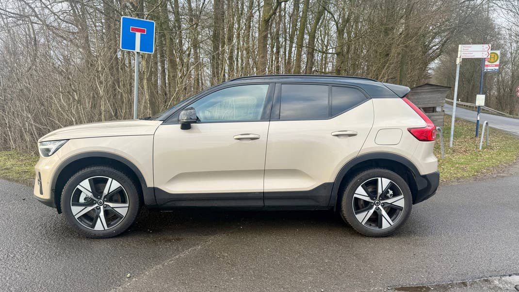A side view of a Volvo EX40 parked near a road sign and trees.
