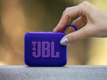 A hand holding a purple JBL Go 4 portable speaker on a surface.