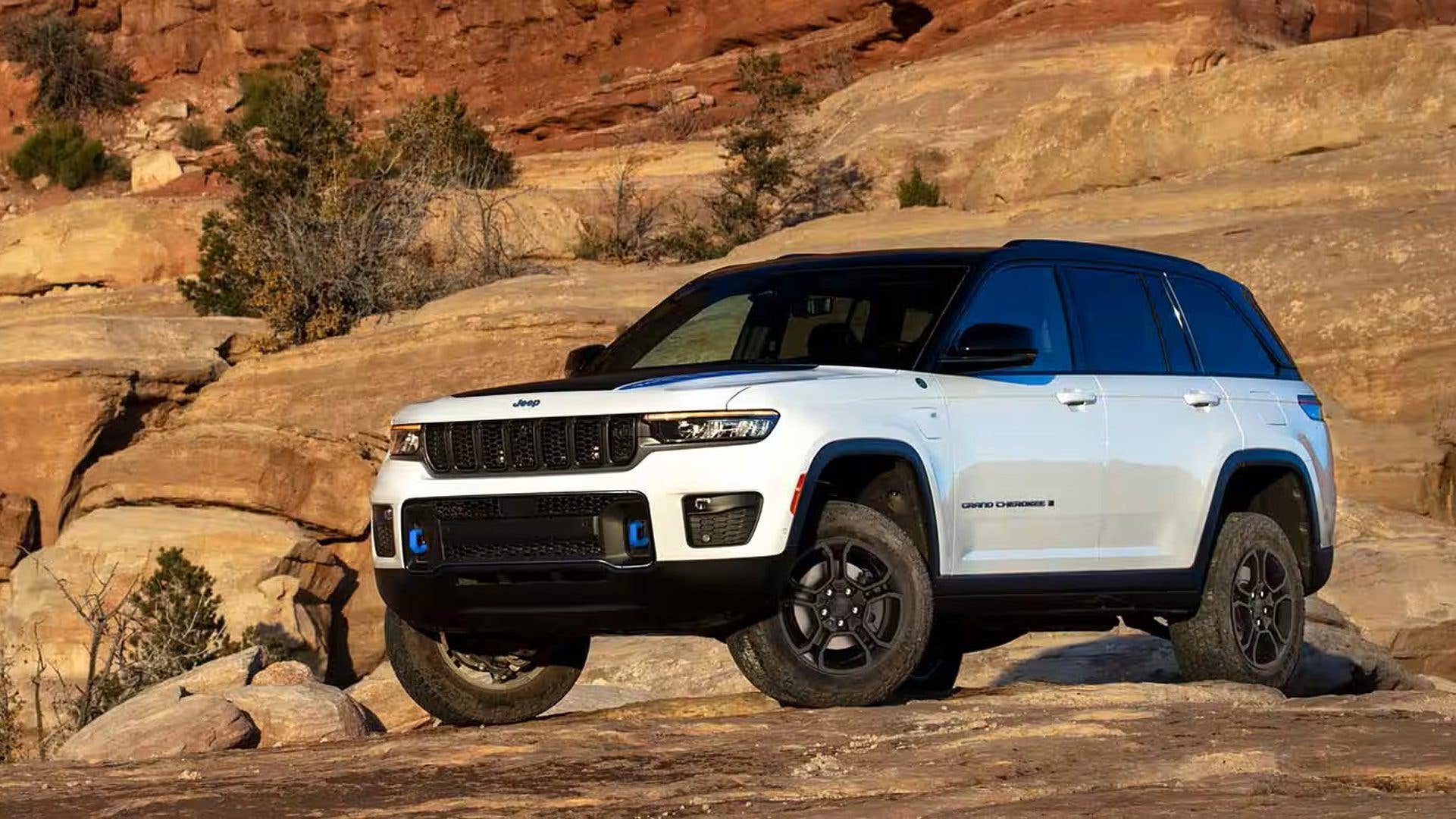 A white Jeep SUV parked on rocky terrain with red cliffs in the background.
