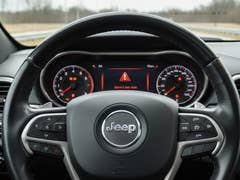 Interior view of a Jeep steering wheel and dashboard with warning lights.