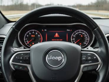 Interior view of a Jeep steering wheel and dashboard with warning lights.