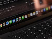 Close-up of a laptop screen showing Google Chrome icon on the dock with coding text in the background.