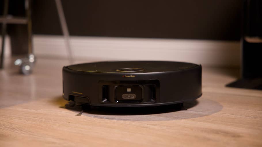 A black robot vacuum cleaner on a wooden floor, labeled 'AI Smart Sight'.