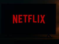 A dark room featuring a TV displaying the Netflix logo in red.