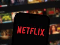 Netflix logo on smartphone screen, Netflix home screen in the background.