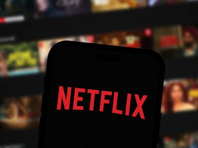 Netflix logo on smartphone screen, Netflix home screen in the background.