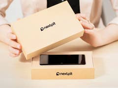 A person unboxing a new smartphone from a NextPit-branded box on a table.
