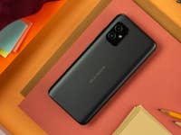 The back of an ASUS Zenfone 8 smartphone on a colorful background of papers and stationery.