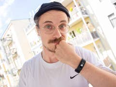 A person with glasses and a mustache holds their chin, wearing a Garmin Vivosmart 5 smartwatch.