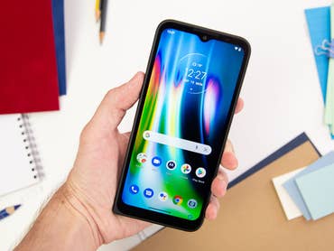 A person holding a Motorola Defy smartphone displaying the home screen.