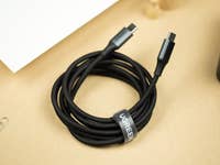 A Ugreen 140W charger with a black USB-C cable coiled next to it on a beige surface.