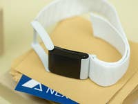 A black fitness tracker with a white strap on a stack of envelopes and a blue card.