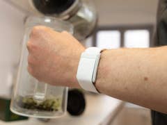A hand holding a glass teapot with a white smartwatch on the wrist.